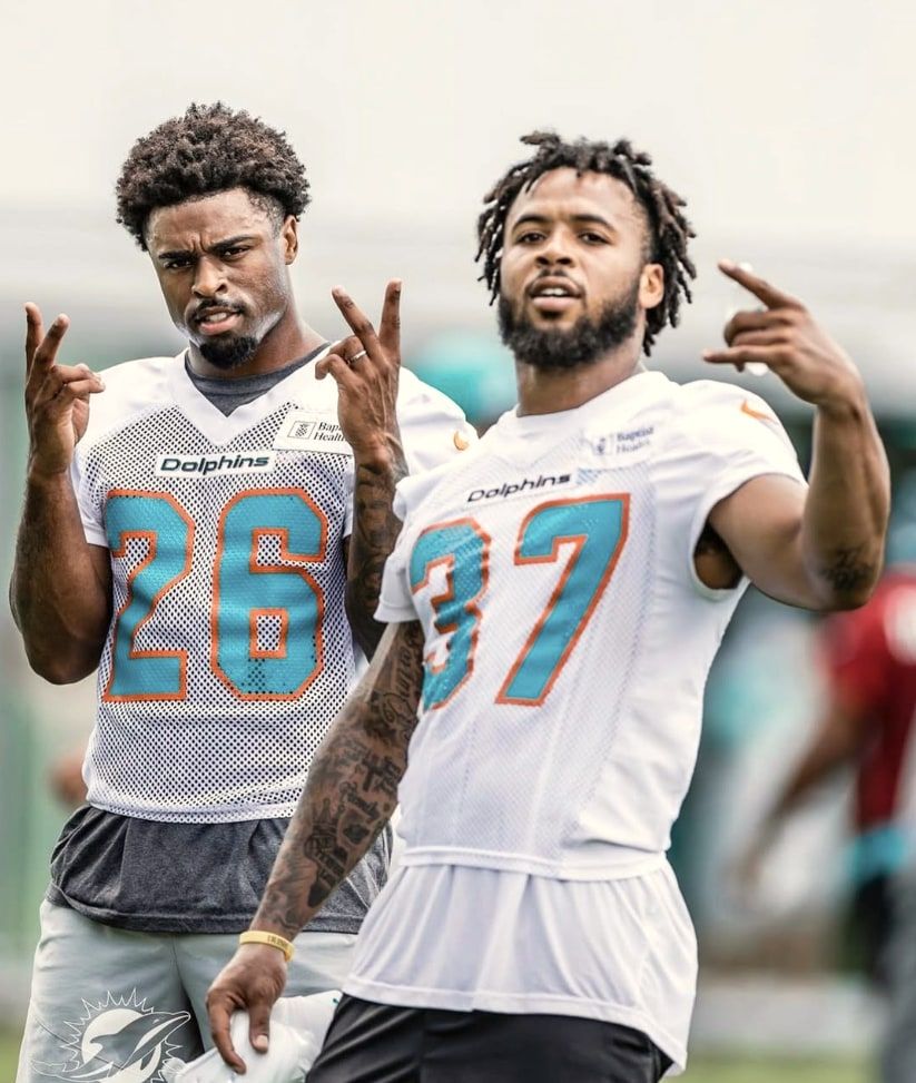 Salvon Ahmed and Myles Gaskin in Miami Dolphins practice jerseys, numbers 26 and 37, each throwing up a hand sign at the camera