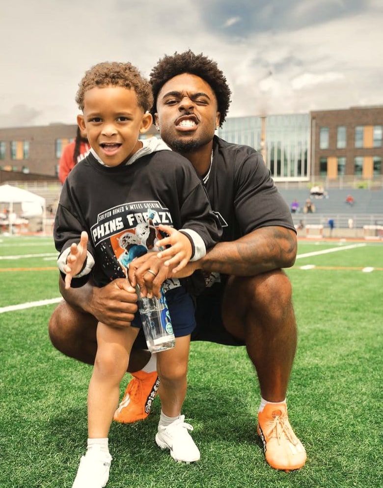 Salvon Ahmed crouches with a young camper in a camp shirt, both smiling at the camera