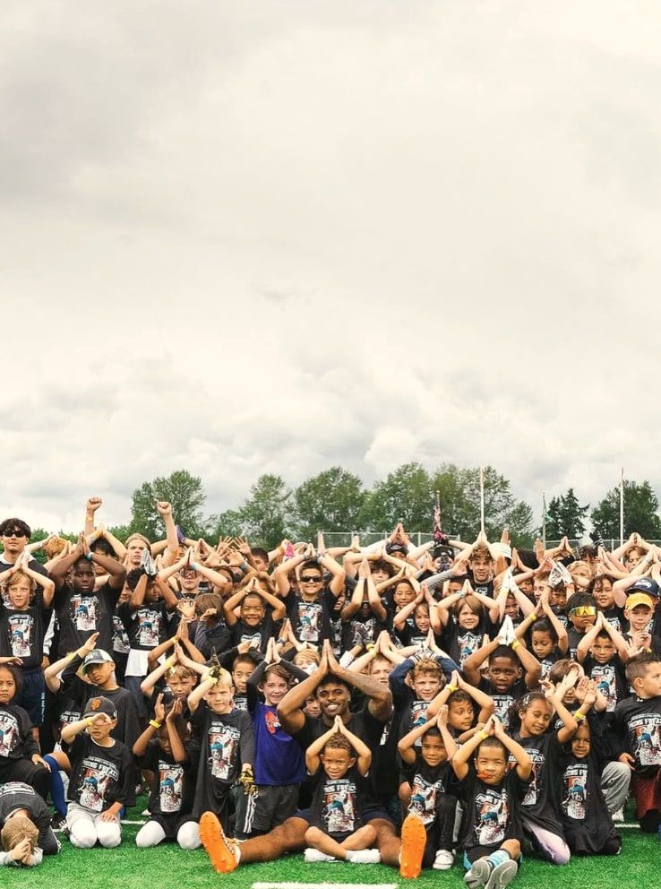Campers on the field for the group photograph, most of them making the fins hand sign, Salvon seated in the middle