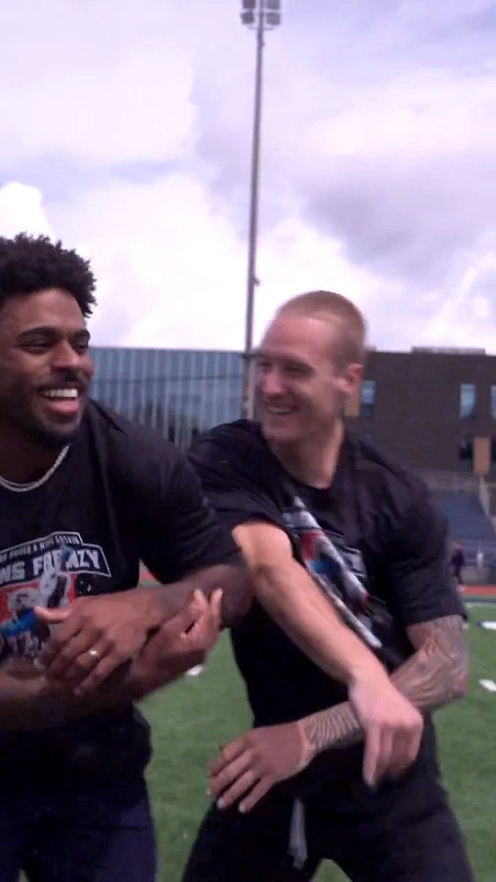 Salvon laughing with a friend on the field, both in camp shirts, the school behind them